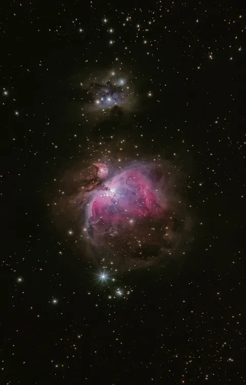 Pink and blue nebula glowing amid a dense field of stars in deep space