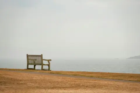 Empty wooden bench facing a calm, hazy sea